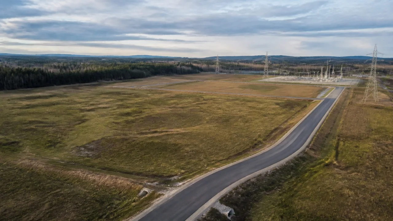 Open ground beside an access road and electrical substation, before site work begins